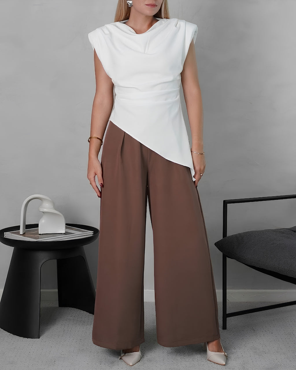 una mujer con blusa asimetrica de hombreras blanca y pantalon marron