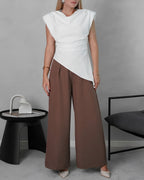 una mujer con blusa asimetrica de hombreras blanca y pantalon marron