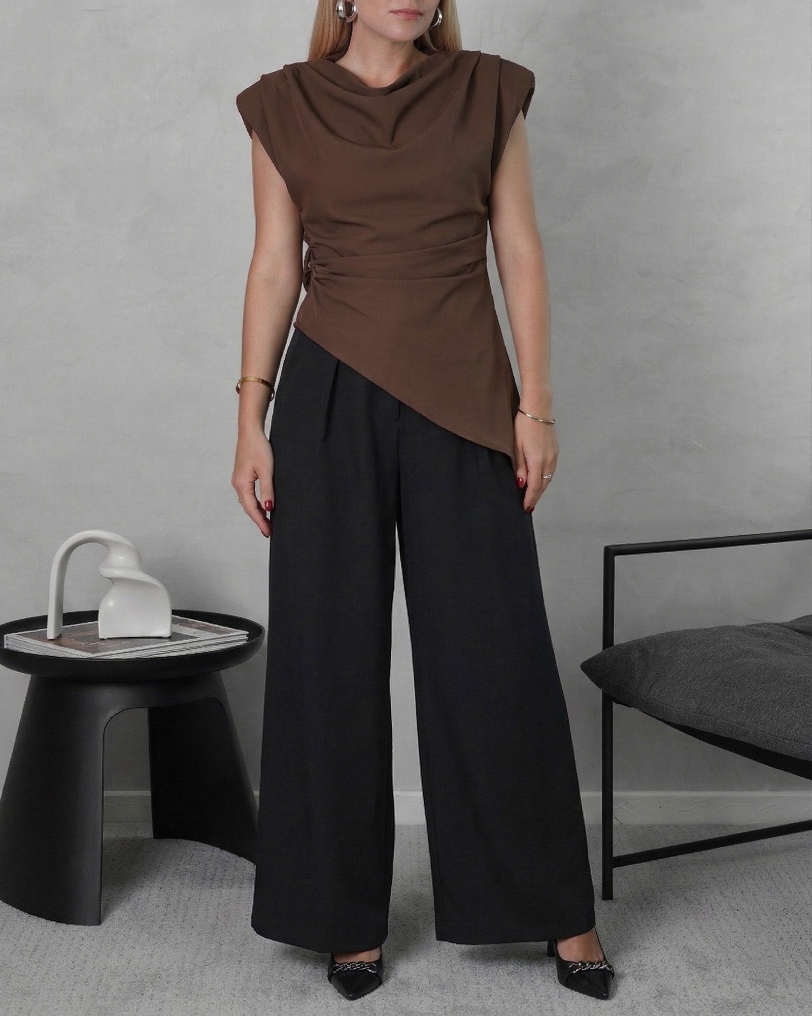 una mujer con blusa asimetrica de hombreras marron y pantalon negro