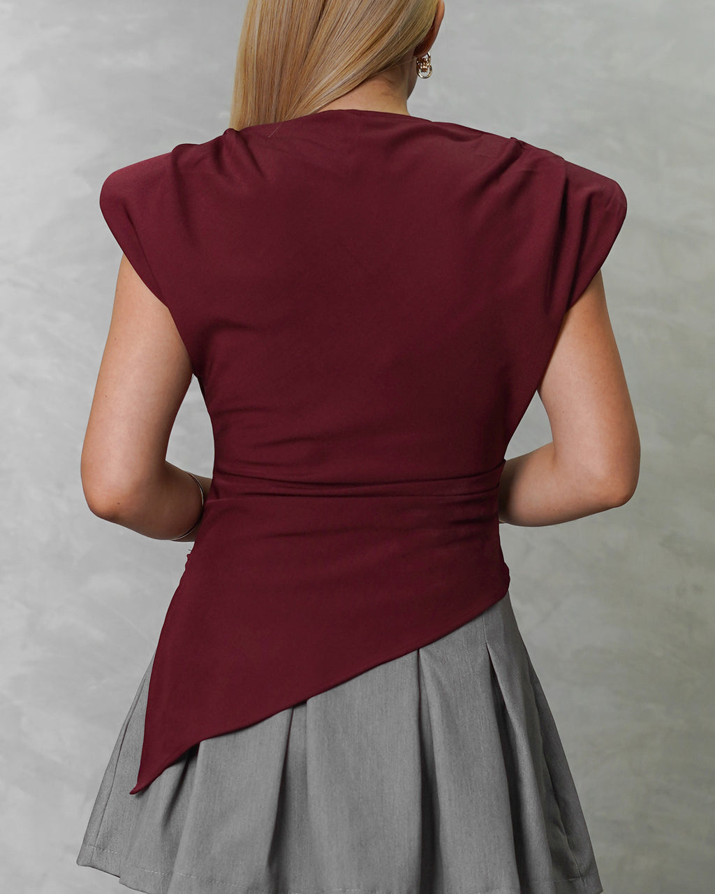  una mujer de espalda con blusa asimetrica de hombreras vinotinto