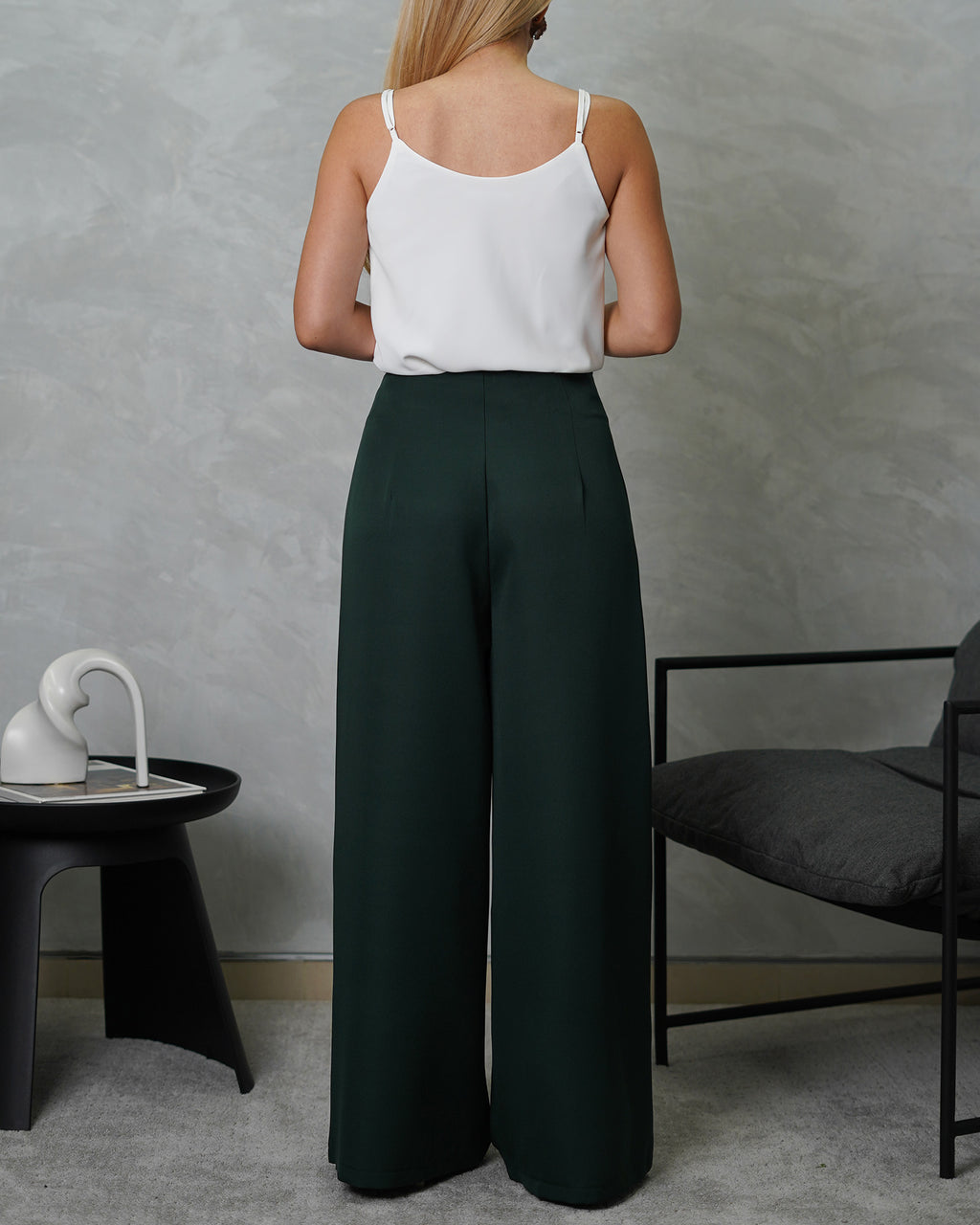 una mujer de espalda con una blusa básica de tiras cuello V blanca y pantalon verde oscuro