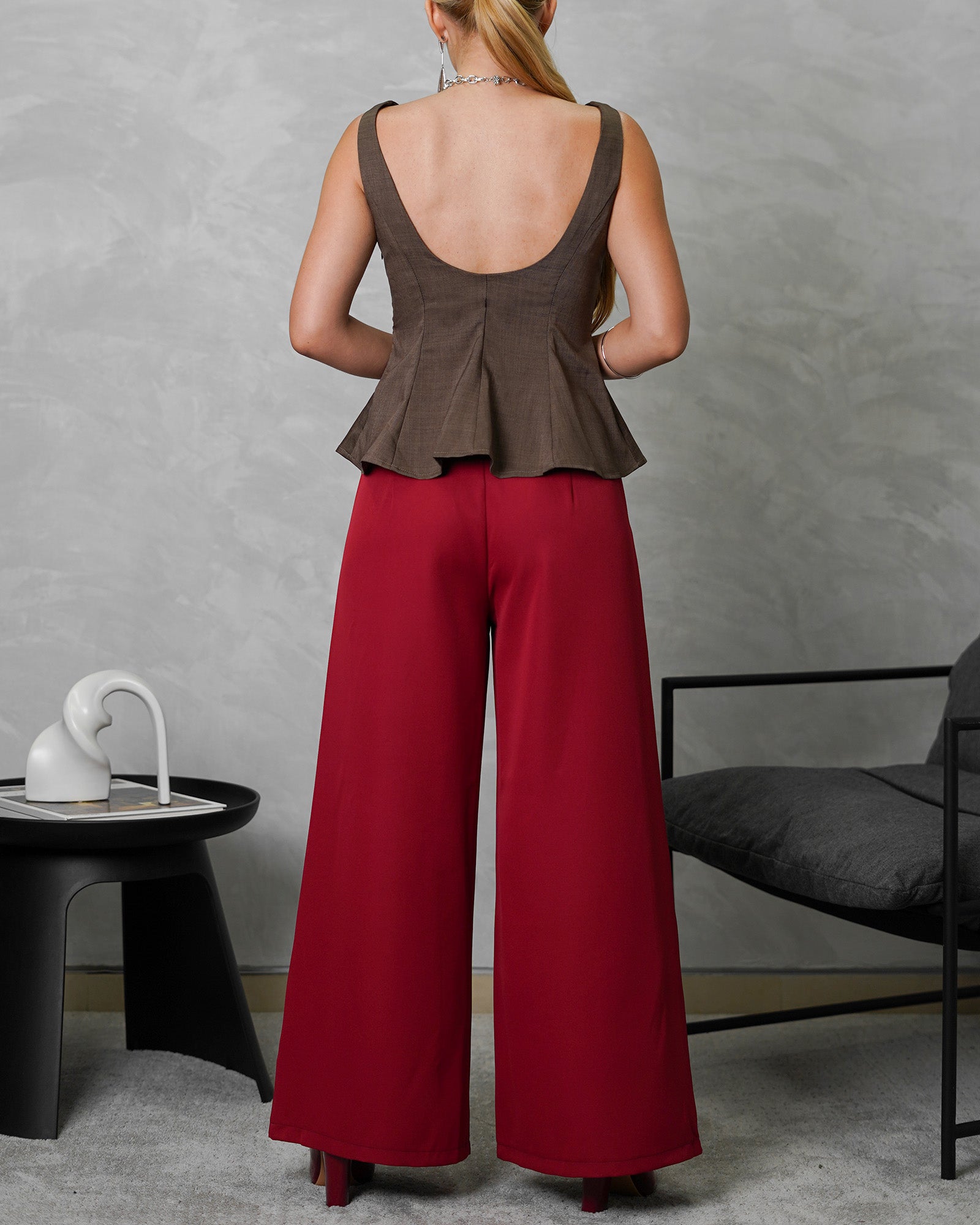 mujer de espalda de cuerpo completo usando blusa campanada de espalda escotada marron y pantalon vinotinto