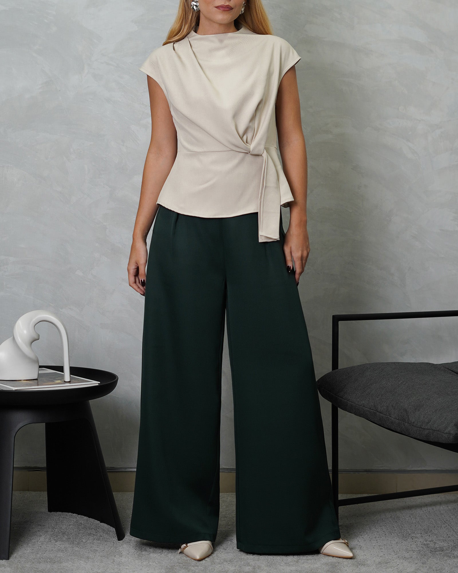 una mujer con blusa campanada de tira colgante beige y pantalon verde oscuro