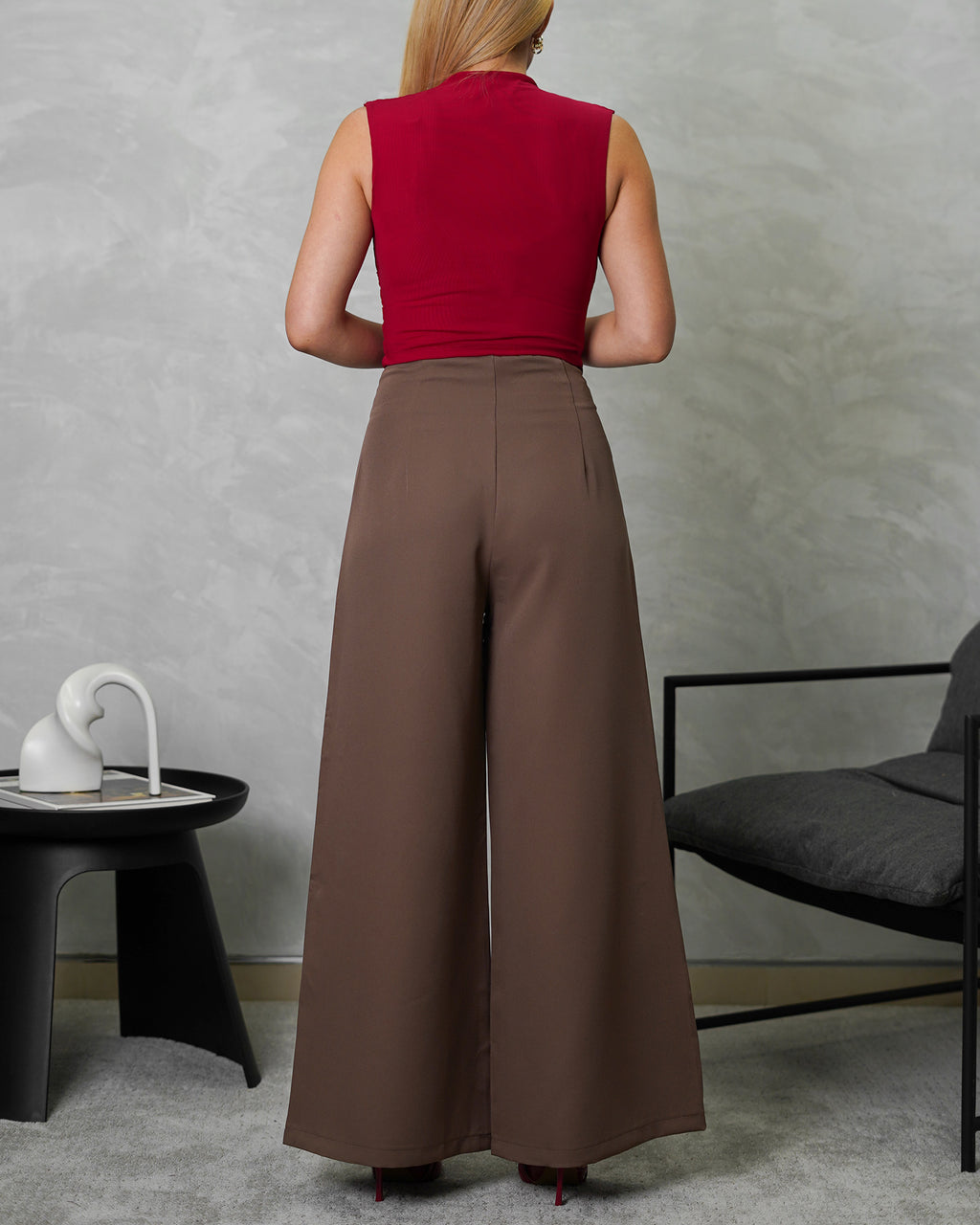 una mujer de espalda con blusa de corte bajo en v vinotinto y pantalon marron