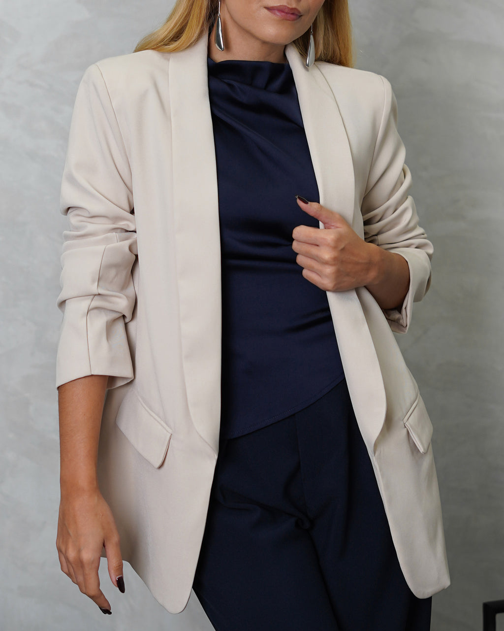 Una mujer con blusa de seda sin mangas cuello asimetrico azul marino y blazer beige