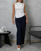 Una mujer con blusa de seda sin mangas cuello asimetrico blanco y pantalon azul marino
