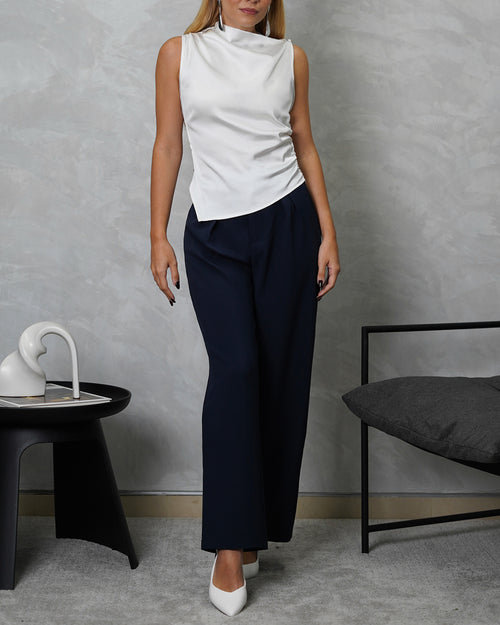 Una mujer con blusa de seda sin mangas cuello asimetrico blanco y pantalon azul marino