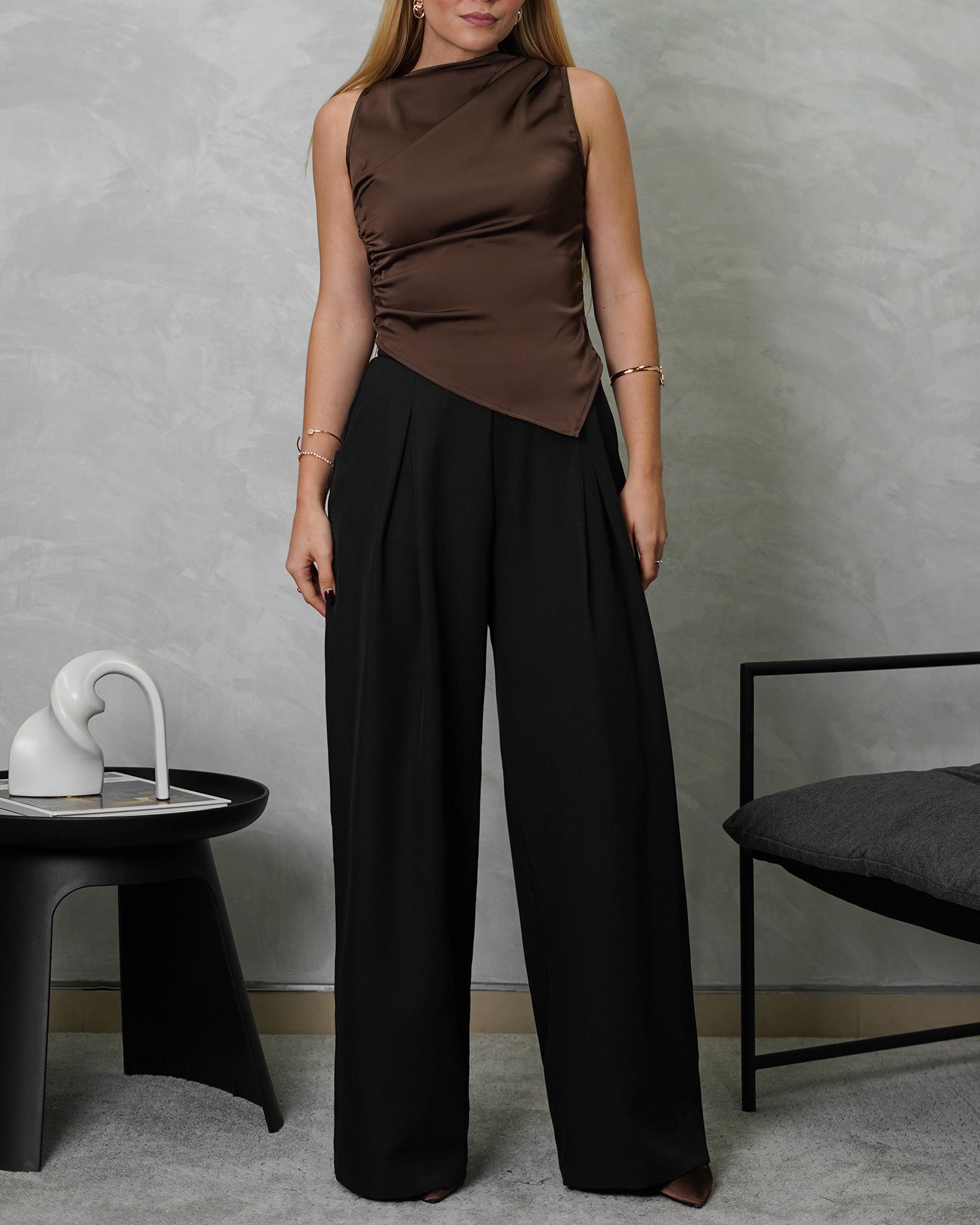 Una mujer con blusa de seda sin mangas cuello asimetrico marron y pantalon negro