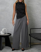 Una mujer con blusa de seda sin mangas cuello asimetrico negro y pantalon gris