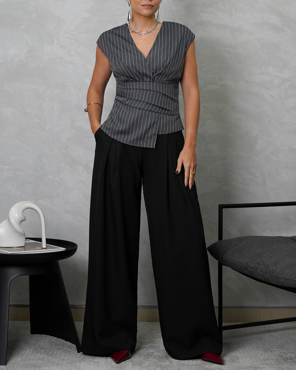 una mujer de cuerpo completo con blusa sin mangas de rayas verticales gris y pantalon negro