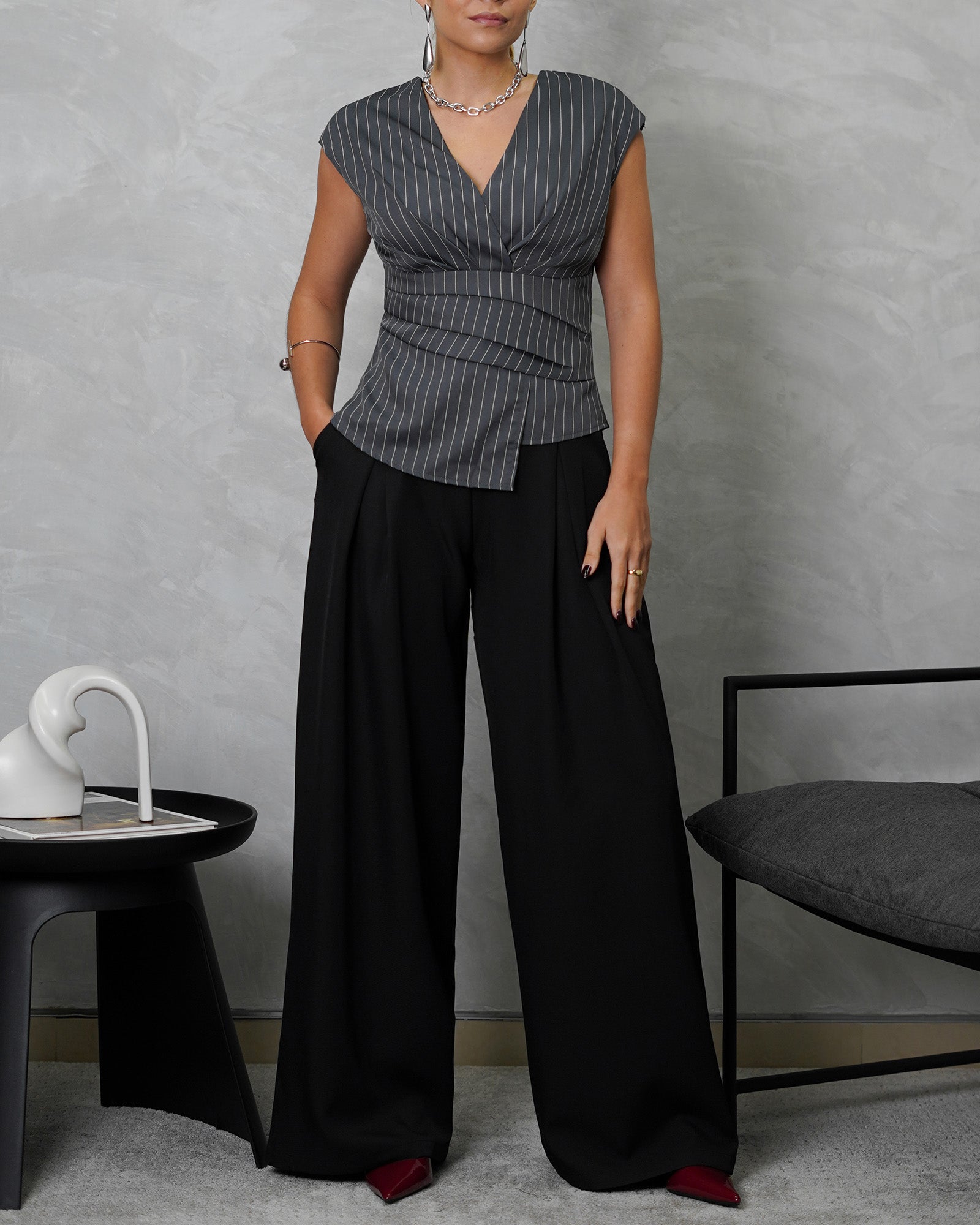 una mujer de cuerpo completo con blusa sin mangas de rayas verticales gris y pantalon negro