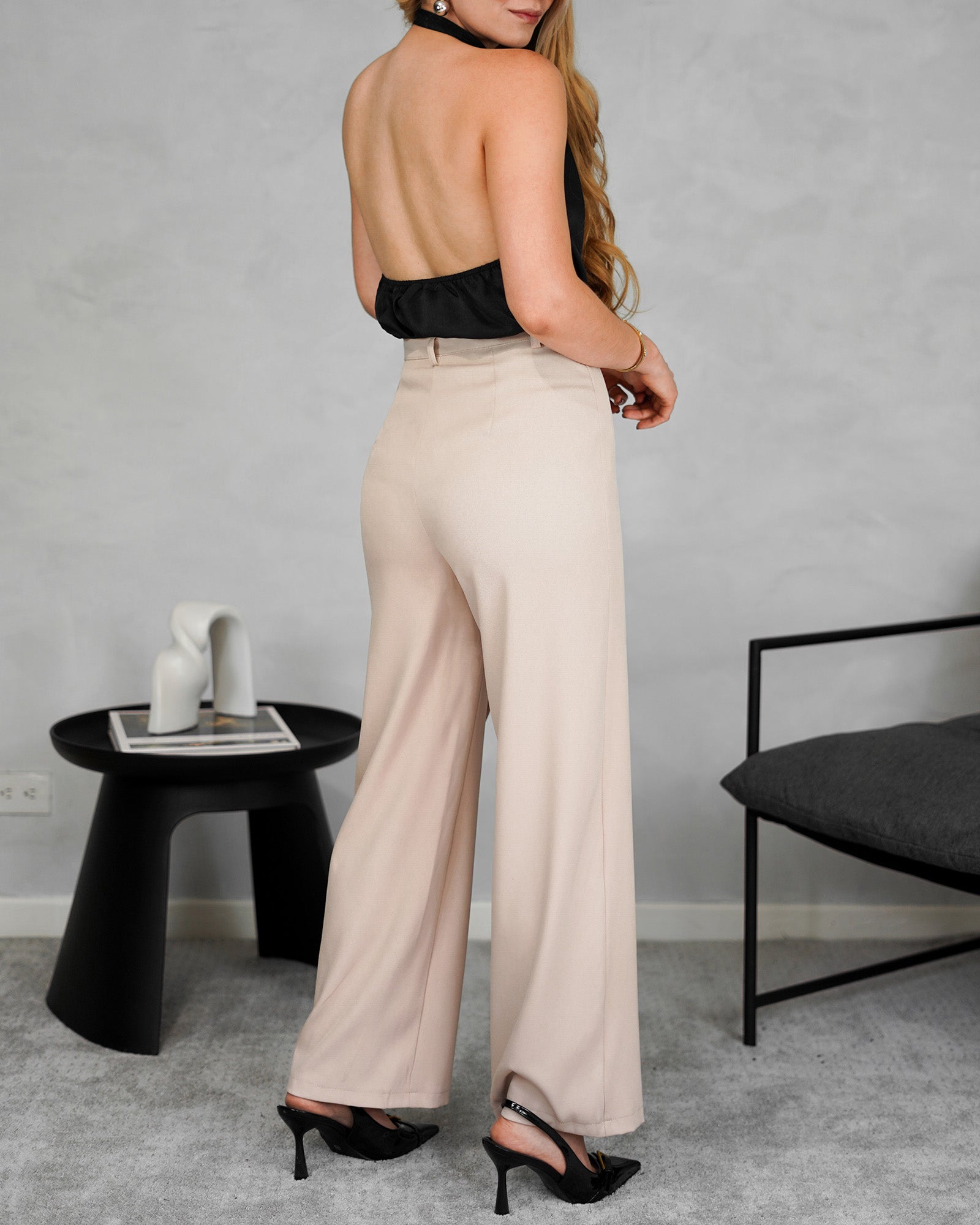 una mujer con una blusa negra sin mangas y espalda abierta y pantalon beige 