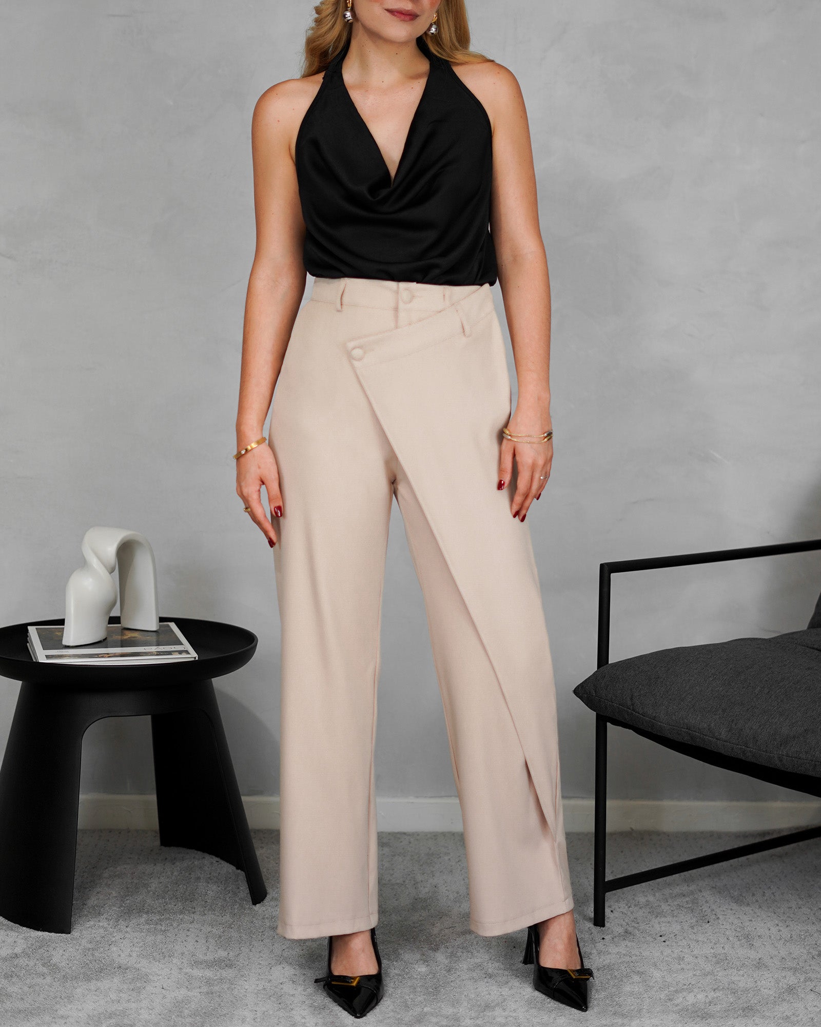 una mujer con una blusa negra sin mangas y espalda abierta y pantalon beige 