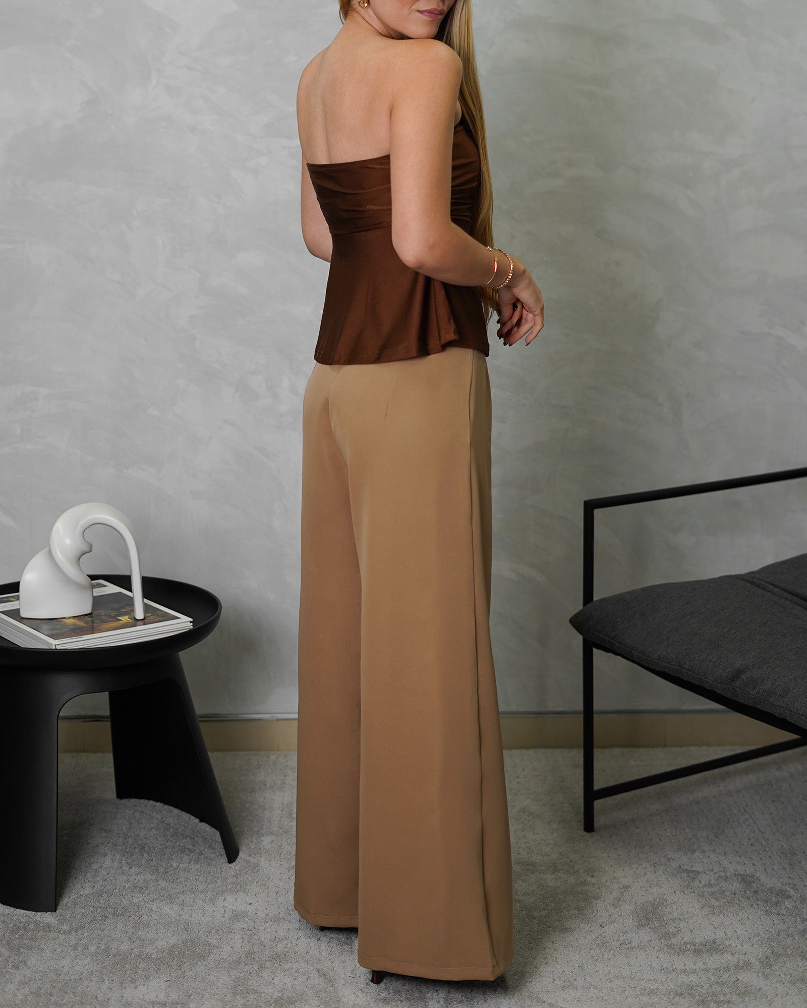una mujer de espalda con blusa strapless campanada marron satinada y pantalon marron claro