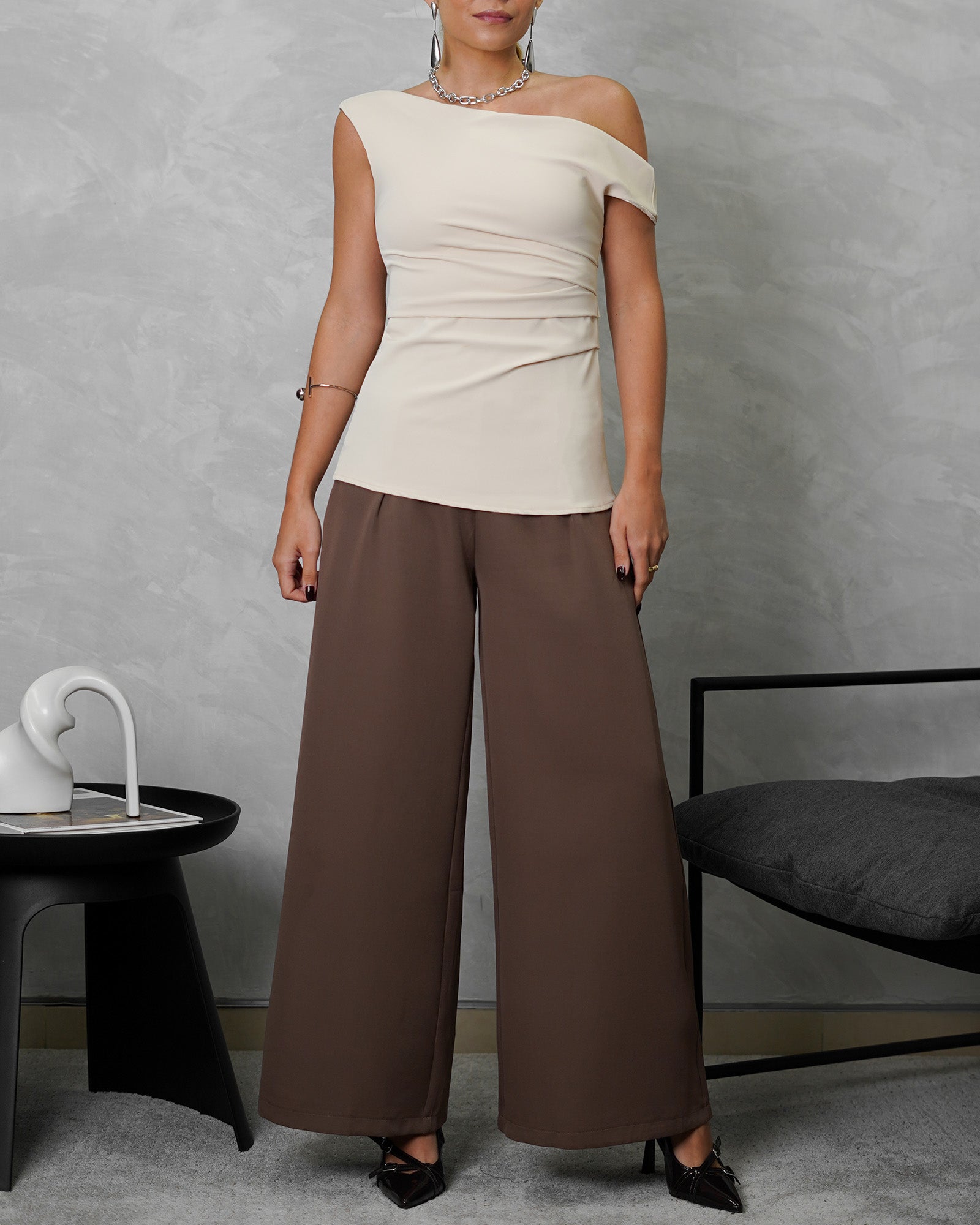 una mujer con blusa de un hombro descubierto beige y pantalon marron