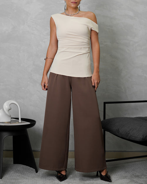 una mujer con blusa de un hombro descubierto beige y pantalon marron