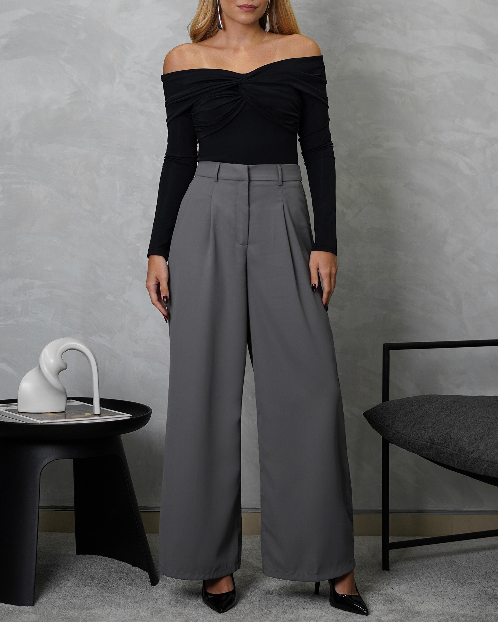 una mujer con un body off shoulder manga larga entrelazado negro y pantalon gris