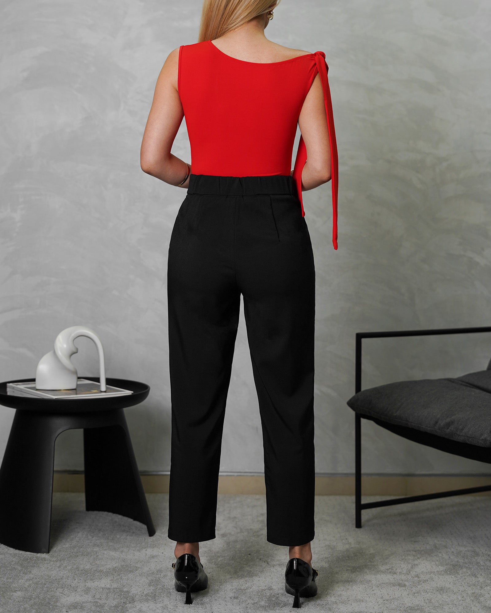 una mujer de espalda con body de tira colgante en el hombro roja y pantalo negro tubo