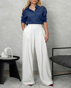una mujer con camisa de botones manga larga oversized azul marino y pantalon blanco