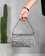 cartera con textura de cocodrilo y solapa asimétrica